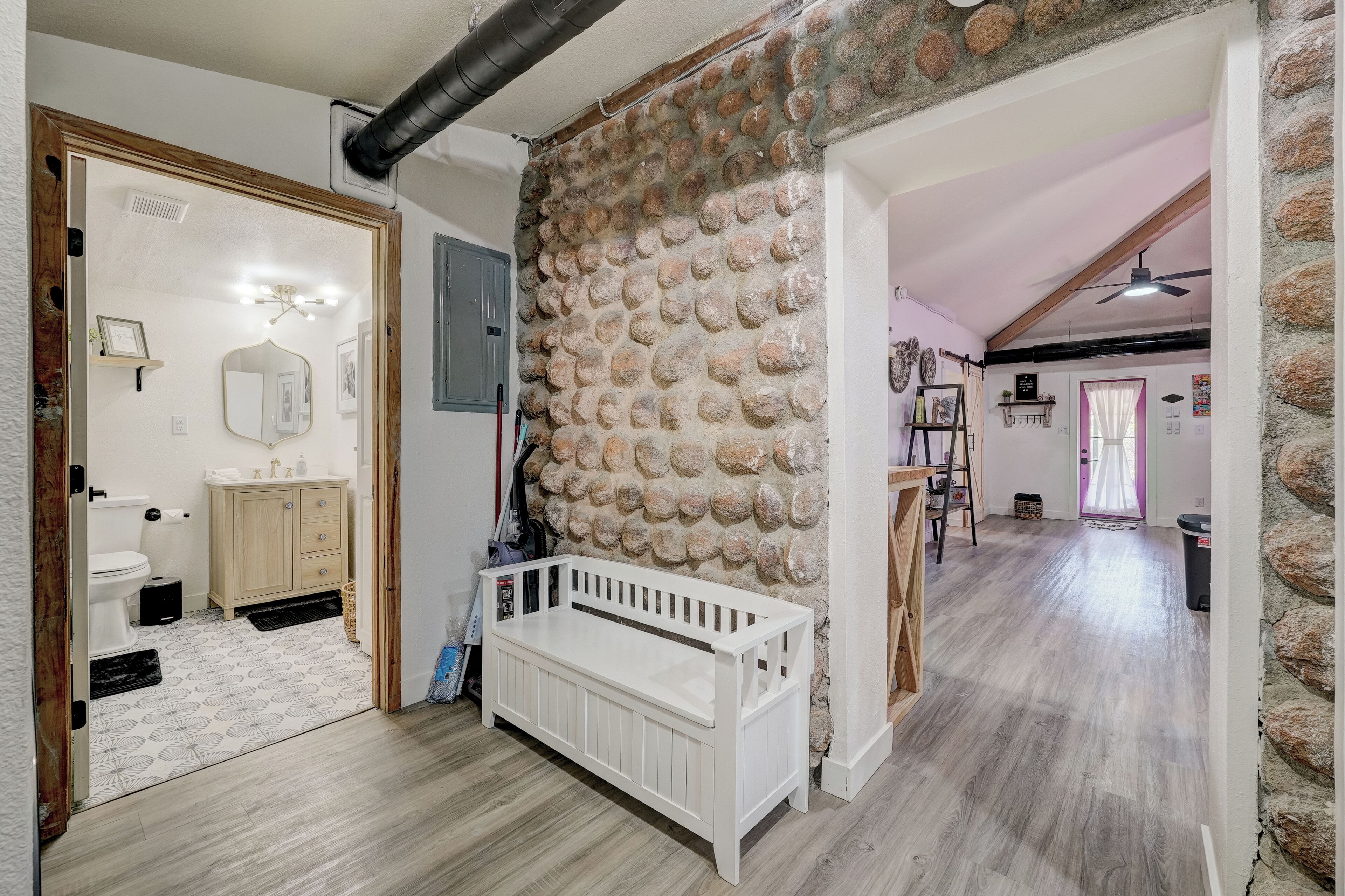 A room with a stone wall, a white bench, a wooden door, and a view into another room.
