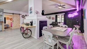 A dining area with a wooden table and white chairs, a pink bicycle, and a brick fireplace.