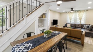 A modern living room with a staircase, a dining area with a wooden table, and a sofa set. - Fantastic retreat 5 mins from Village with media room, AC and sauna! (Stowe)