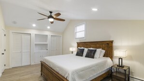 A bedroom with a wooden bed, a ceiling fan, a nightstand with a lamp, and built-in closets. - Fantastic retreat 5 mins from Village with media room, AC and sauna! (Stowe)