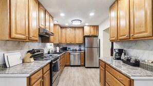 A modern kitchen with wooden cabinets, stainless steel appliances, and a marble countertop. - Fantastic retreat 5 mins from Village with media room, AC and sauna! (Stowe)