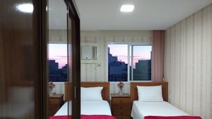 Une chambre d’hôtel avec deux lits, un plancher en bois, une fenêtre donnant sur la ville et un miroir.
