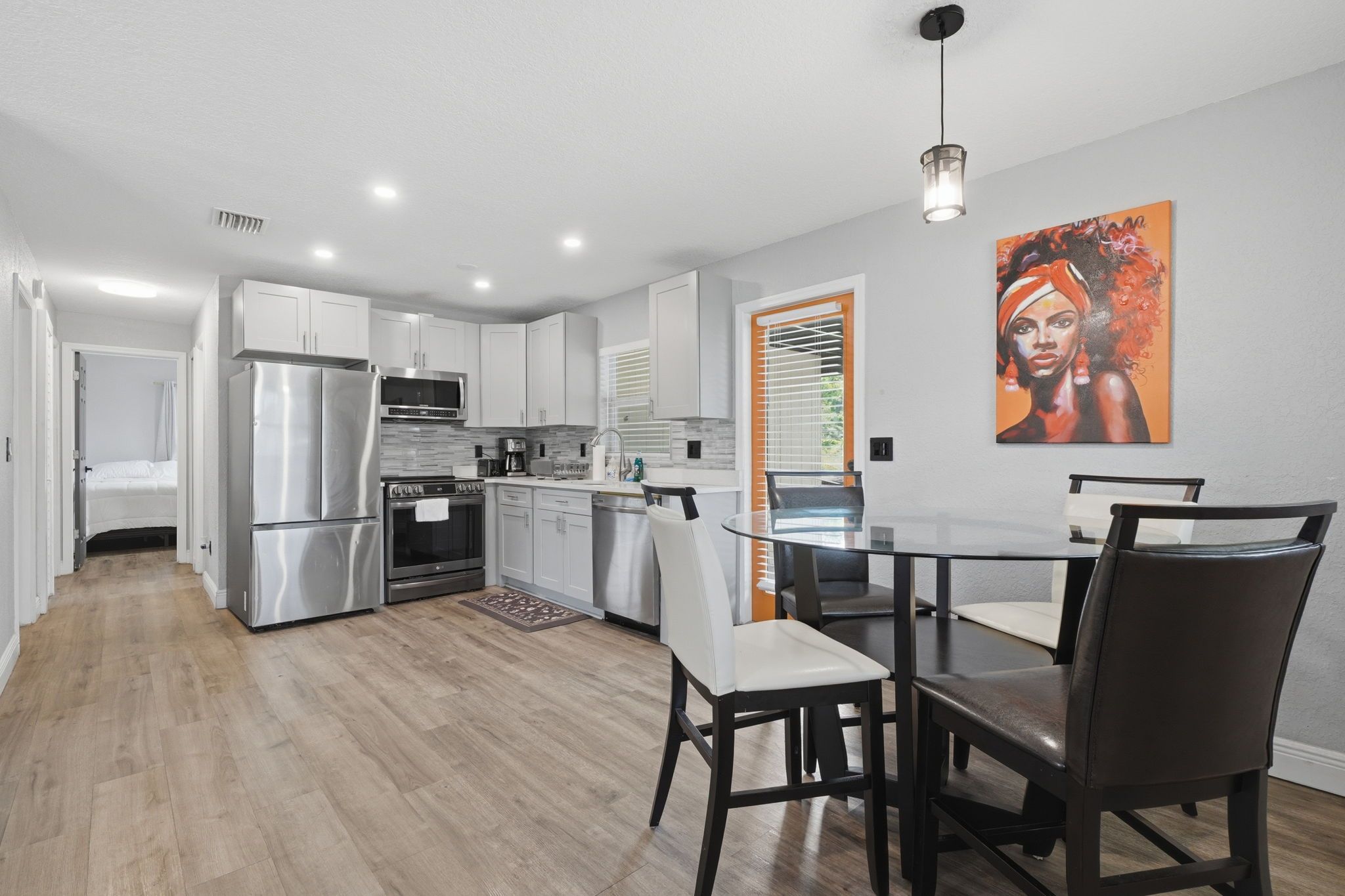 A modern kitchen with stainless steel appliances, a dining area with a table and chairs, and a painting on the wall.