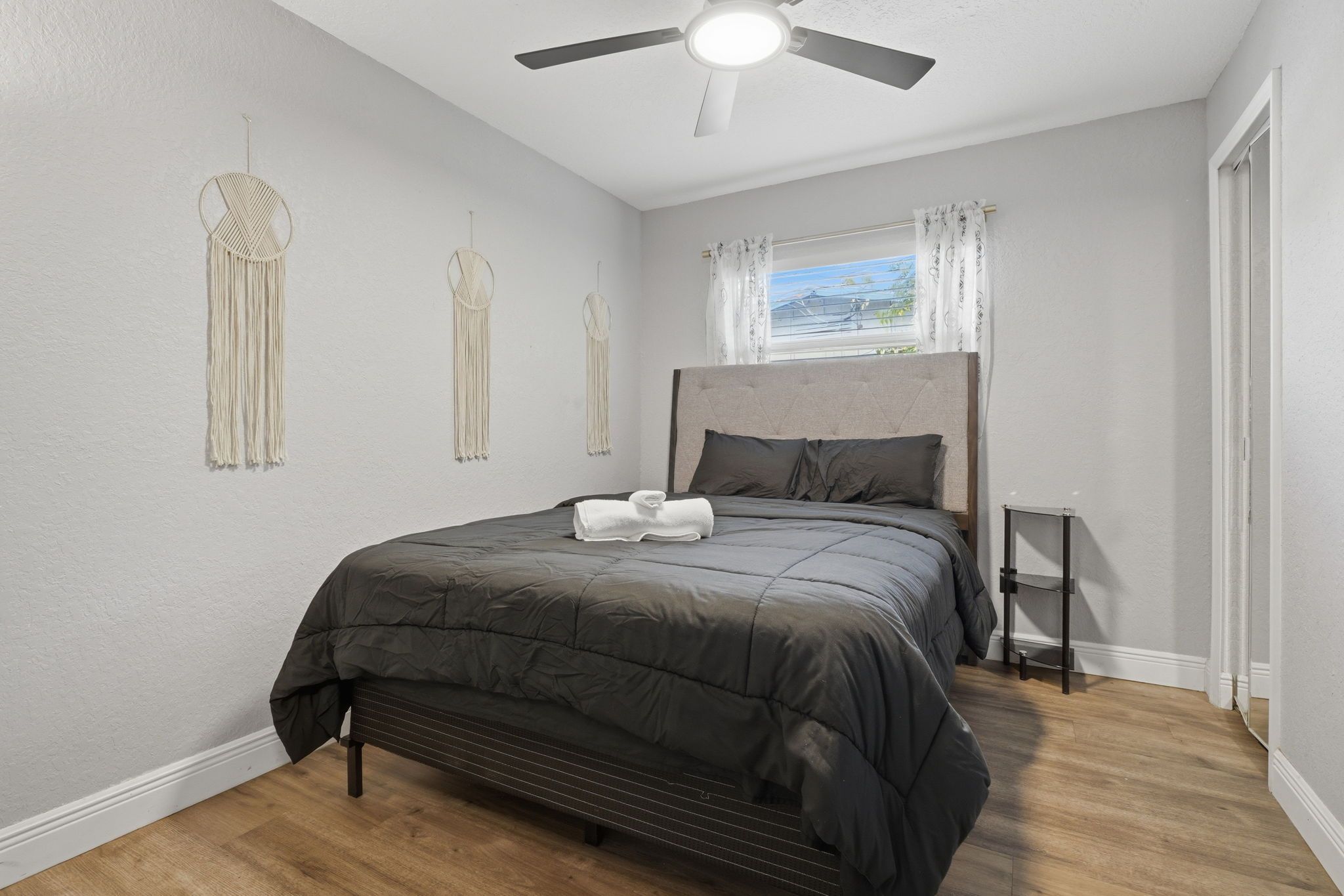 A bedroom with a bed, a ceiling fan, a window with curtains, and wall decor.