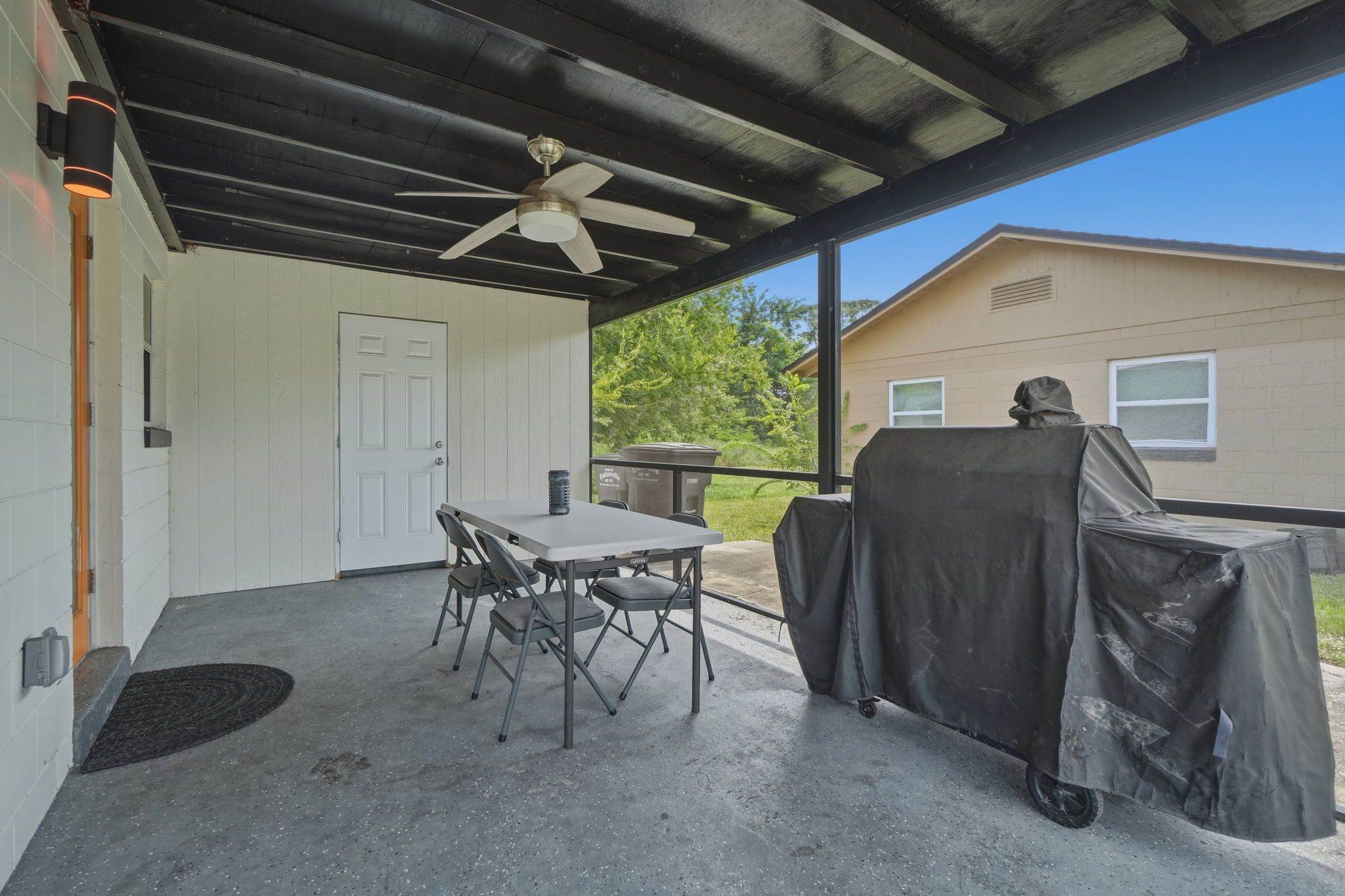 An outdoor patio with a table and chairs, a ceiling fan, and a covered grill area.
