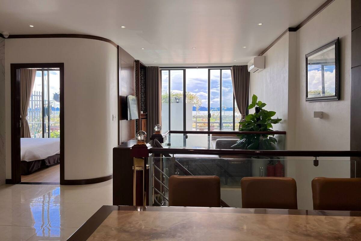 Quarto de hotel com varanda, área de refeições com mesa de mármore e cama com vista para o exterior.
