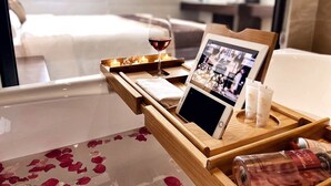 A wooden tray with a tablet, a glass of red wine, and two bottles of lotion on a bed with rose petals. - Elysinam Boutique Hotel (Bai Chay)