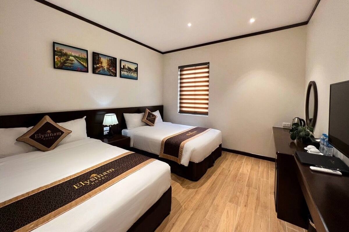 Quarto de hotel com duas camas, uma mesa, televisão e obras de arte na parede.