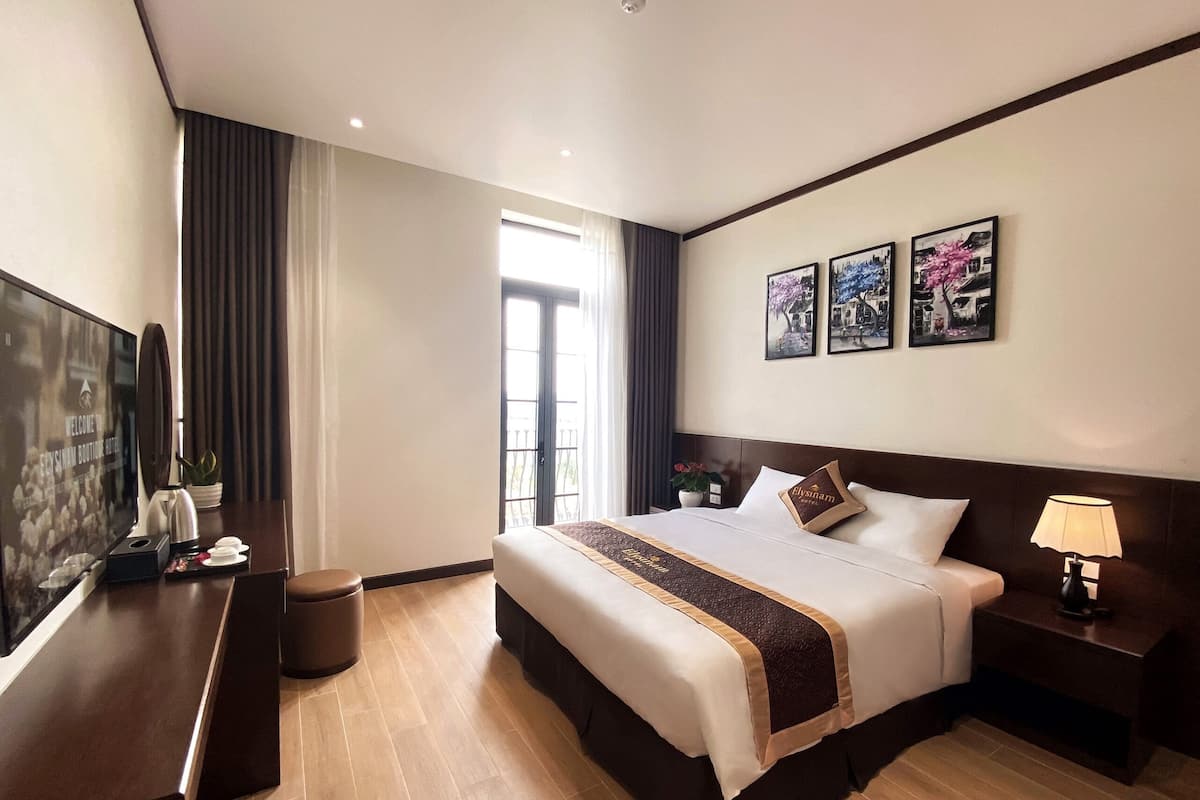 Quarto de hotel com uma cama grande, mesa de cabeceira com abajur, televisão e vista para o exterior.