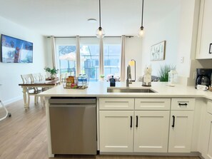 A modern kitchen with a dishwasher, white cabinets, and a dining area with a table and chairs.