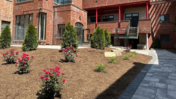 Un edificio de ladrillo de varios pisos con un patio central, con zonas ajardinadas, arbustos y flores.
