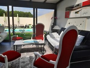 Uma área de estar moderna ao ar livre com piscina, mobiliário vermelho e branco, e vista para a piscina.