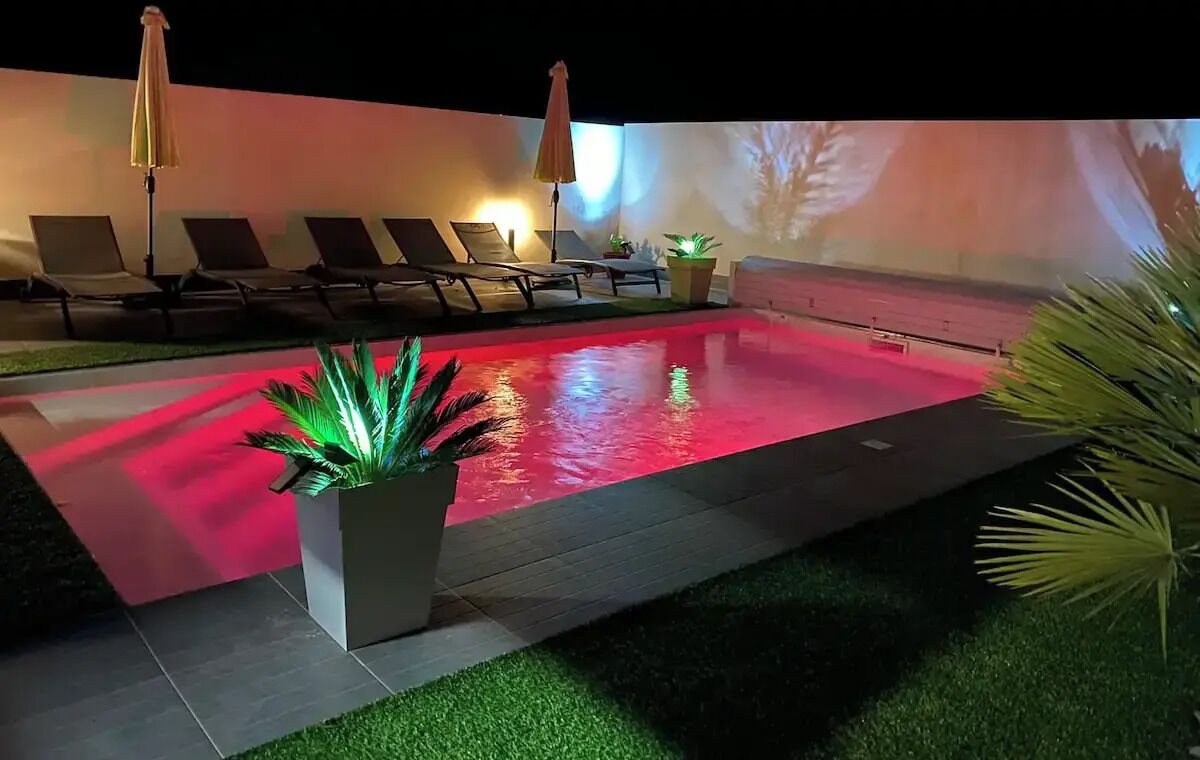 A pool area with lounge chairs and umbrellas, surrounded by a low wall and a projection screen.