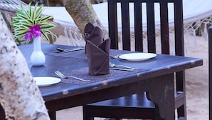 A wooden table set outdoors with a white plate, silverware, and a brown napkin holder. - Jungle Beach Ahungalla - Classic Room (Ahungalla)