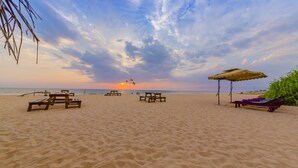 A beach with wooden benches and umbrellas, a clear sky, and the sun setting in the distance. - Jungle Beach Ahungalla - Classic Room (Ahungalla)