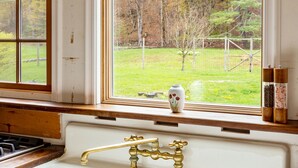 A kitchen with a double sink, wooden cabinets, and a window with a view of a grassy yard and trees. - Catskill dreamy pet friendly country house  for a unique getaway experience. (Claryville)