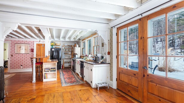 A spacious kitchen with wooden floors, a dining area with a red chair, and a large wooden door with windows. - Catskill dreamy pet friendly country house  for a unique getaway experience. (Claryville)