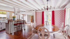A dining area with a wooden table and chairs, a kitchen area with a bar, and a large window with red curtains. - Catskill dreamy pet friendly country house  for a unique getaway experience. (Claryville)