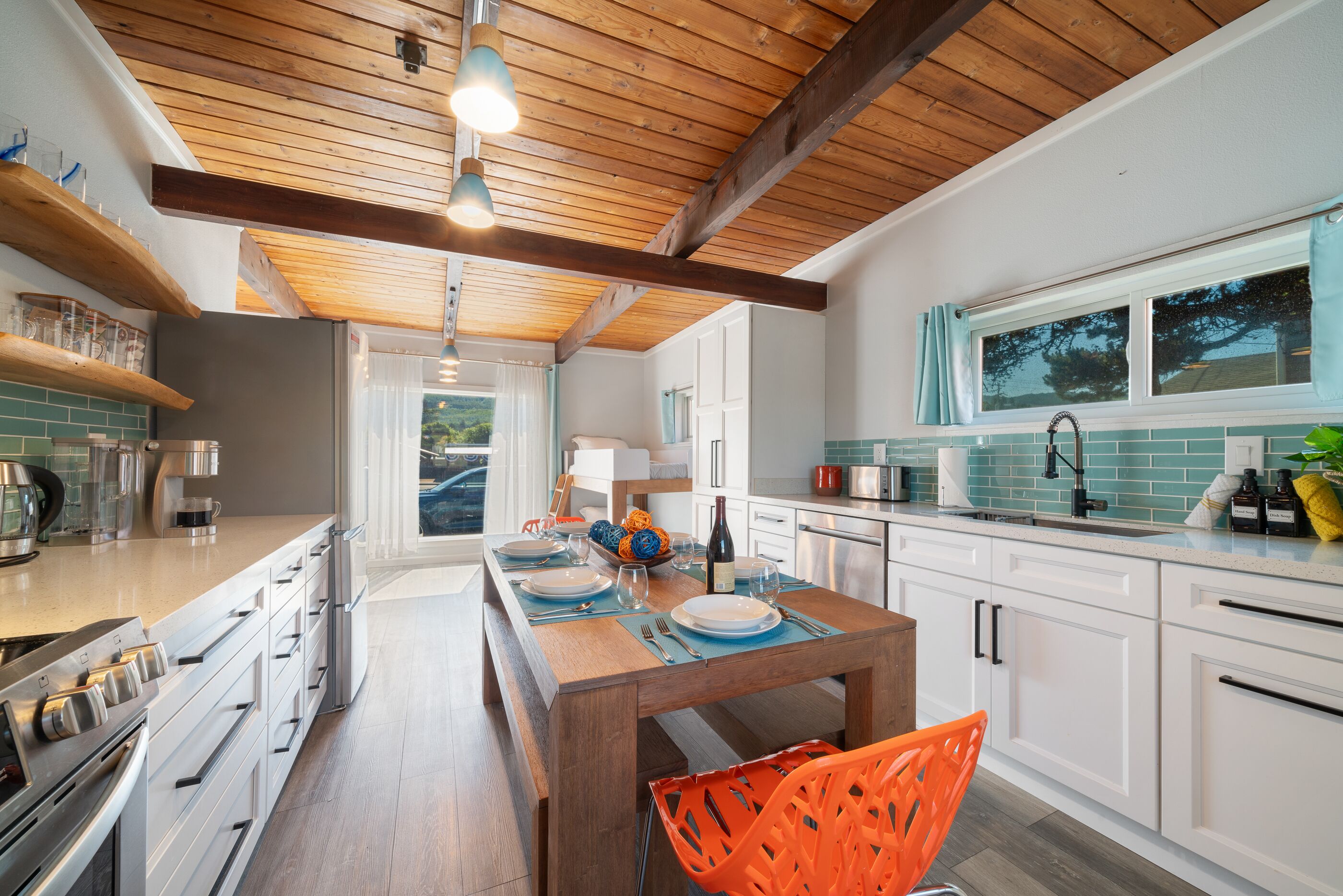 A modern kitchen with wooden beams, white cabinets, and a dining area with orange chairs.