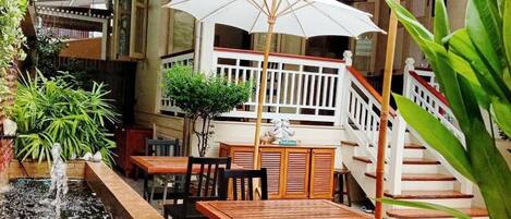 An outdoor seating area with wooden tables and chairs, a small water feature, and white umbrellas.