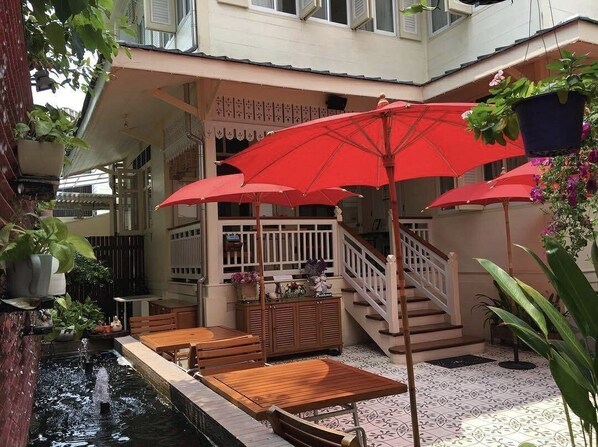 A courtyard with a small pool, wooden furniture, red umbrellas, and potted plants.