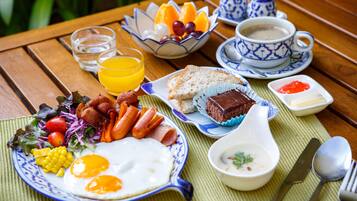 Et morgenbord med æg, bacon, pølser, grøntsager, en skål med frugt, ristet brød, en kop kaffe og et glas appelsinjuice.