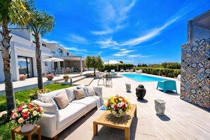 A modern outdoor living area with a pool, a white sofa, and a coffee table. - La Valle Dei Tempi  (Agrigento)