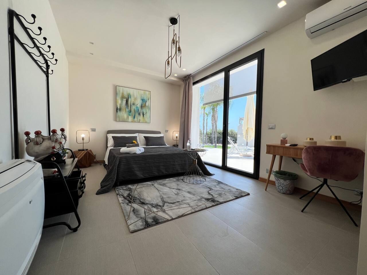 A modern bedroom with a bed, a desk, a chair, a large window, and an air conditioning unit.