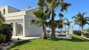Una casa moderna con fachada blanca, césped cuidado y varias palmeras.