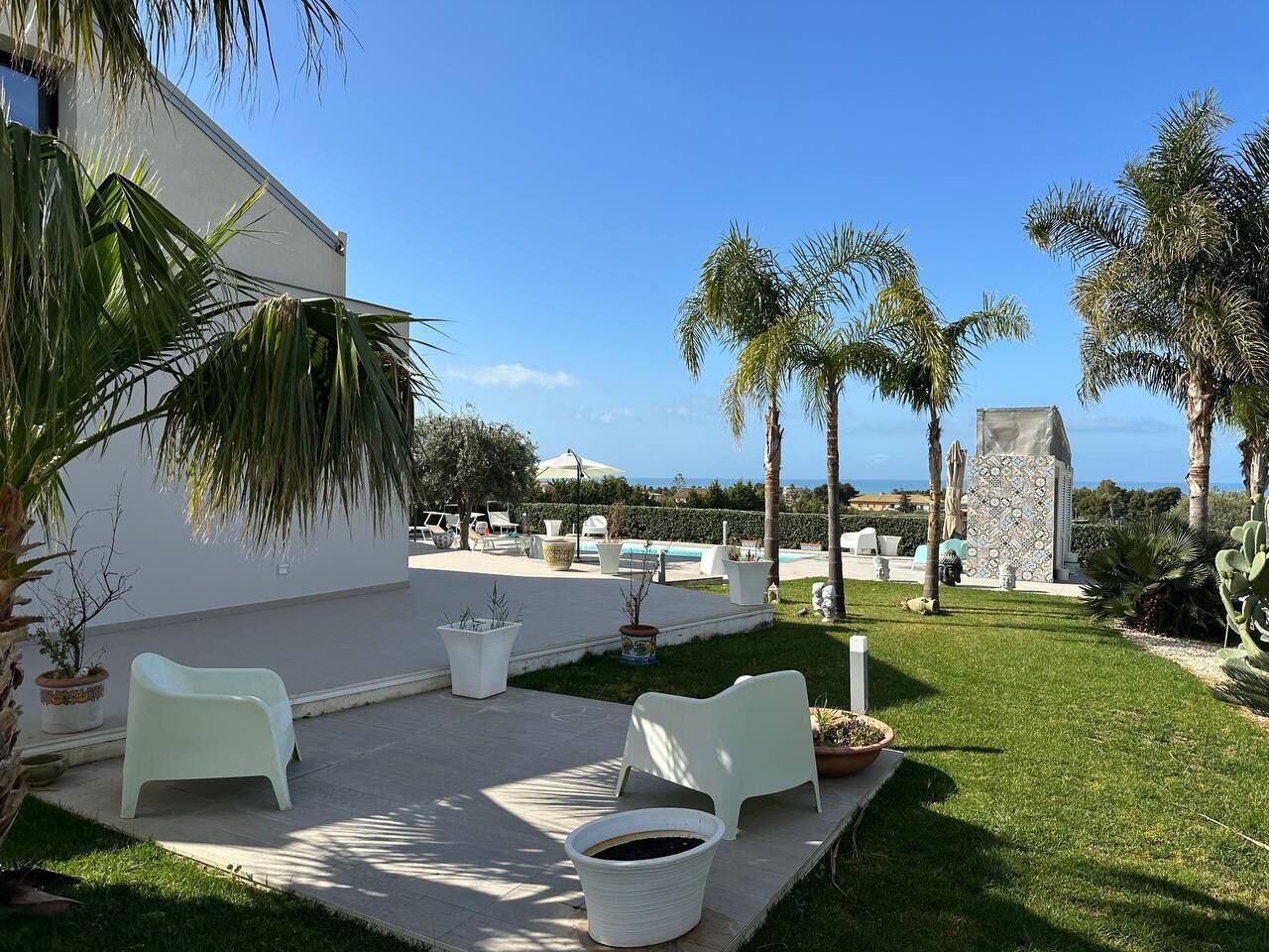 A patio area with outdoor furniture, palm trees, and a view of the sea.