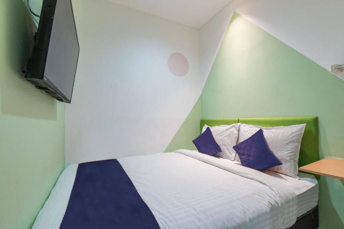 Een bed met een groen hoofdeinde, witte beddengoed en twee blauwe kussens.