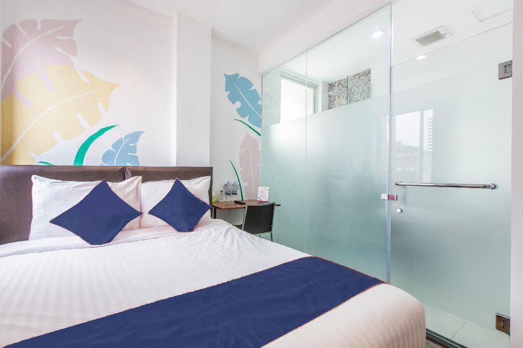 A hotel room with a large bed, a desk, and a glass shower enclosure.