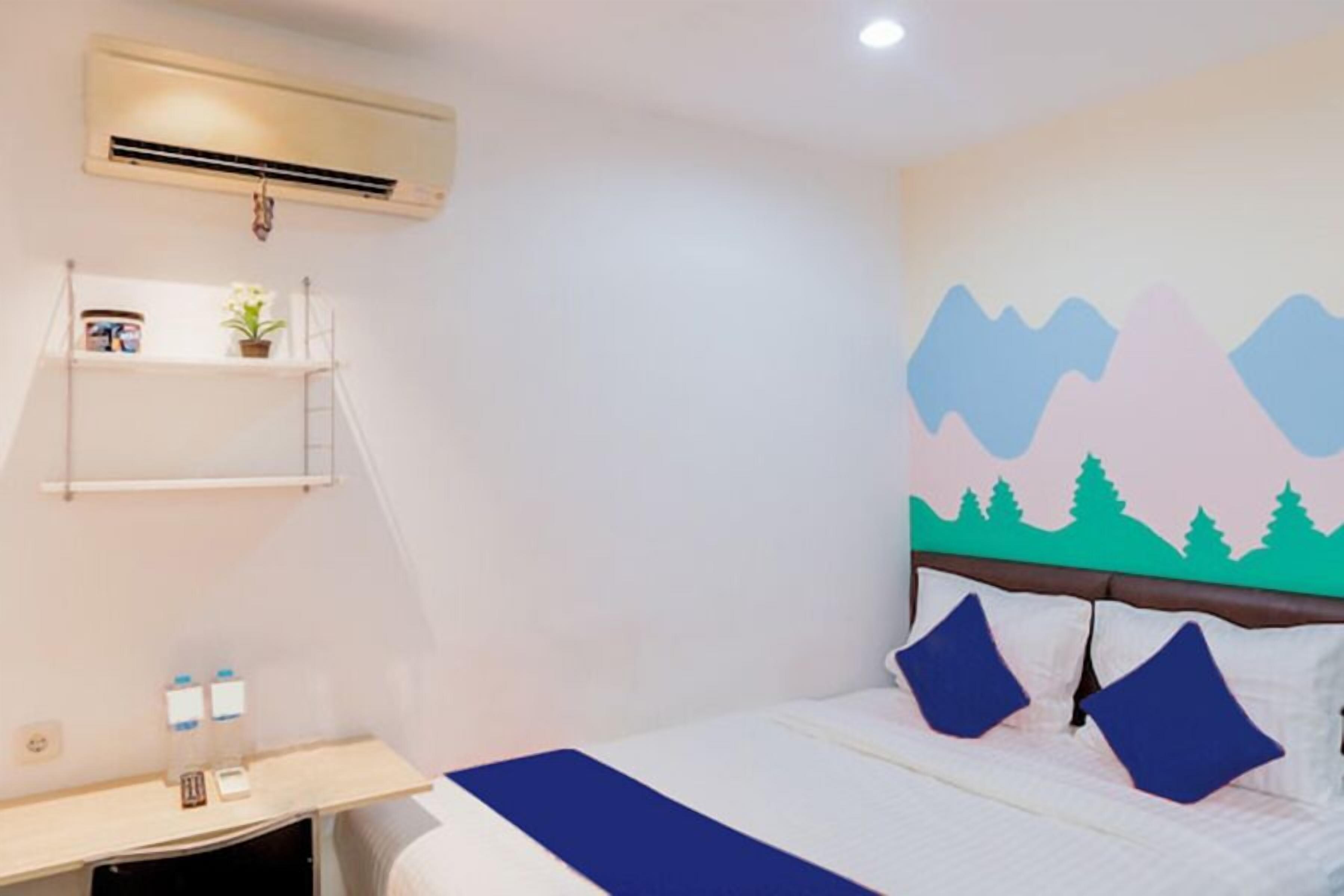 A hotel room with a bed, a nightstand, a shelf with items, and a wall with a mountain design.