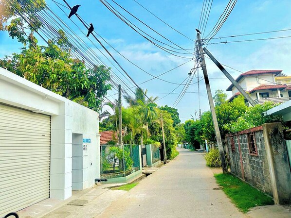 Una calle estrecha bordeada de edificios residenciales, con líneas eléctricas aéreas y algunos pájaros volando.