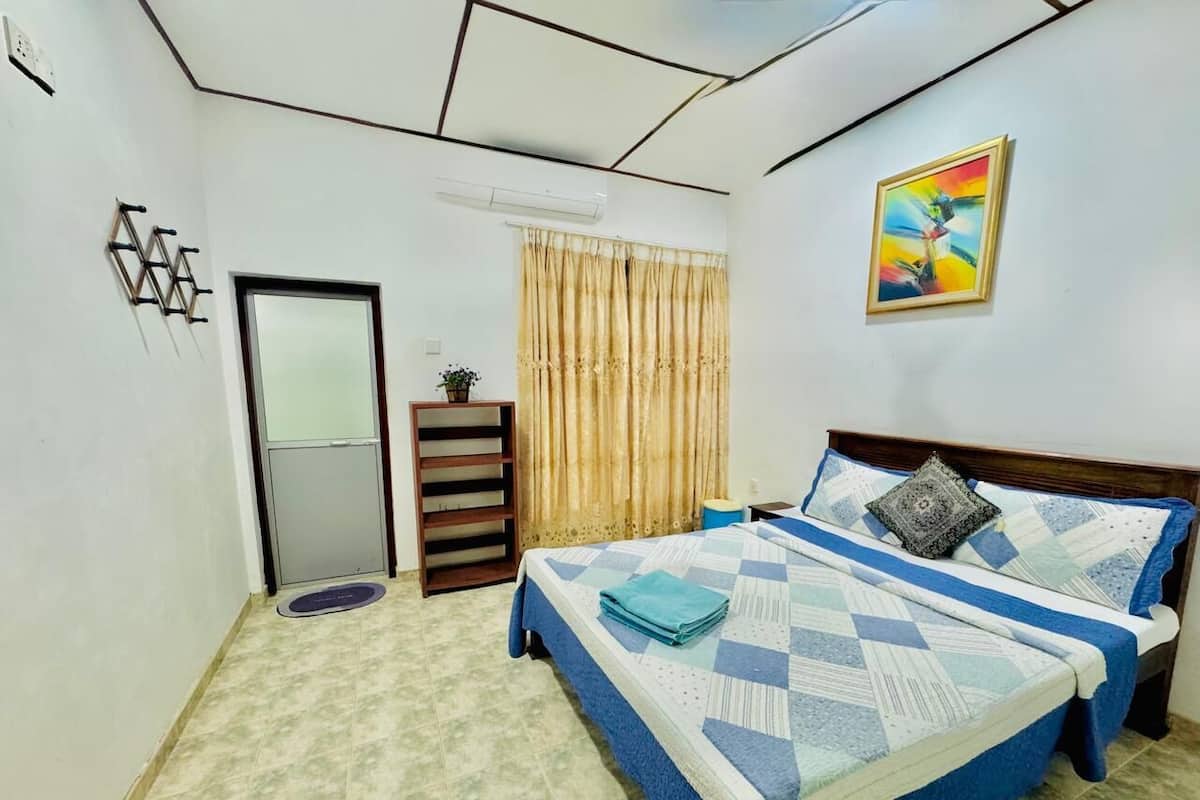 Une chambre à coucher comprenant un lit, une armoire, une petite table, un miroir et une fenêtre avec des rideaux.