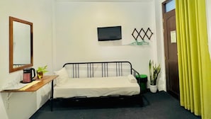 A small, neatly arranged room with a bed, a desk with a mirror, a television, and a door with curtains. - Sea Breeze (Negombo)