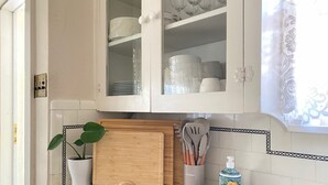 Una cocina con armarios blancos, una tabla de cortar de madera, una planta en maceta y una ventana con cortina.