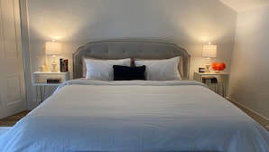 Una cama bien hecha con un cabecero capitonado, dos mesitas de noche con lámparas y una planta junto a la cama.
