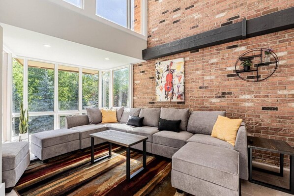 A modern living room with a sectional sofa, a coffee table, and a brick wall with a painting.
