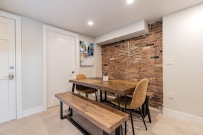 A dining area with a wooden table and benches, a brick accent wall, and a door to the left.