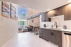 Una cocina moderna con pared de ladrillo, una zona de comedor con sofá y sillas, y un ventanal amplio.
