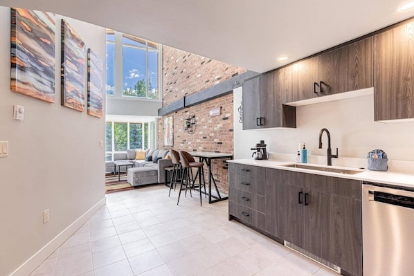 A modern kitchen with a brick wall, a dining area with a sofa and chairs, and a large window.