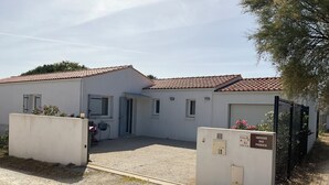 Un bâtiment blanc avec un toit en tuiles, une allée gravillonnée et une zone délimitée par une clôture avec un portail.