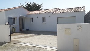 Un bâtiment avec un toit recouvert de tuiles, une allée en gravier et une porte donnant sur un espace abrité.