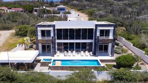 Una moderna casa a due piani con piscina, immersa nel verde e circondata da colline.