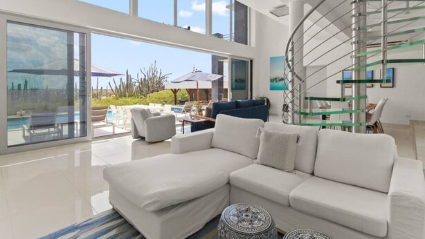 Un soggiorno moderno con un ampio divano angolare bianco, una scala in vetro e vista piscina.