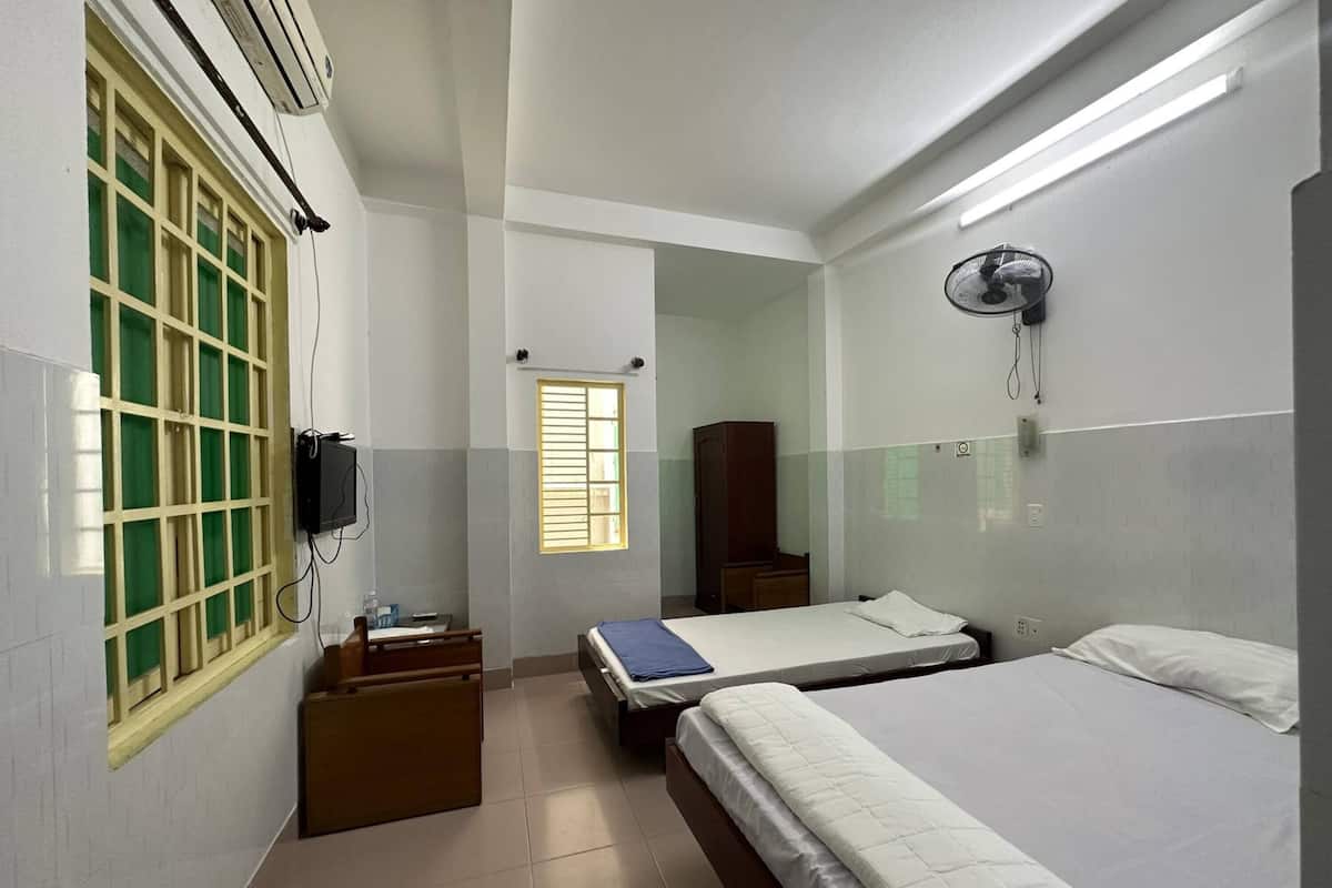 A hotel room with two beds, a small desk, a wardrobe, a mirror, and a window with blinds.