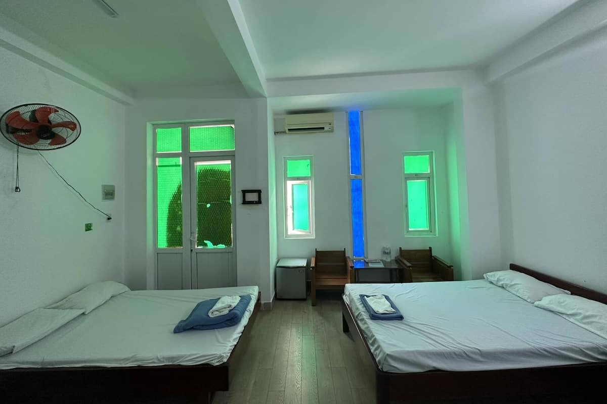 A room with two single beds, a desk, a chair, and a fan.