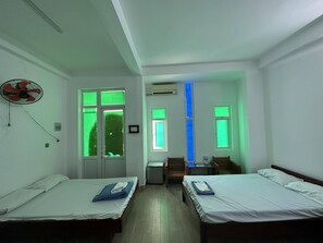 A room with two single beds, a desk, a chair, and a fan.