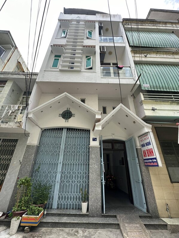 A multi-story building with a gated entrance, a signboard, and potted plants at the entrance.